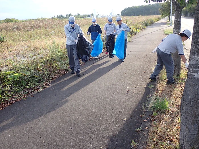 Employees picking up litter along a road during a cleaning activity within the Chitose Rinku Industrial Park.