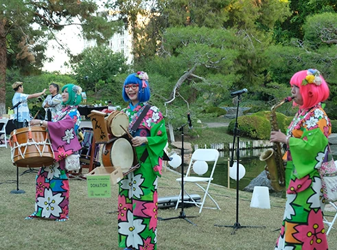 Performers in colorful kimonos playing Wadaiko (Japanese drums) in a Japanese garden.
