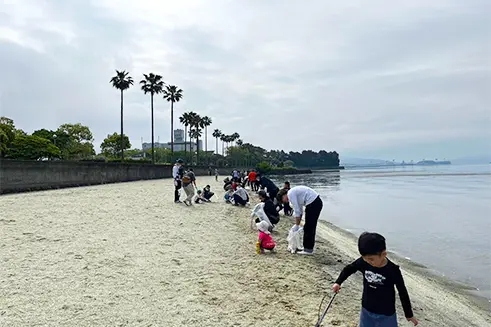 大村湾沿岸の清掃活動で砂浜のゴミ拾いをする参加者たち