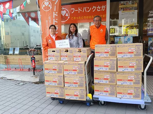 3名の関係者が段ボール箱に入った備蓄水の前で記念撮影している様子